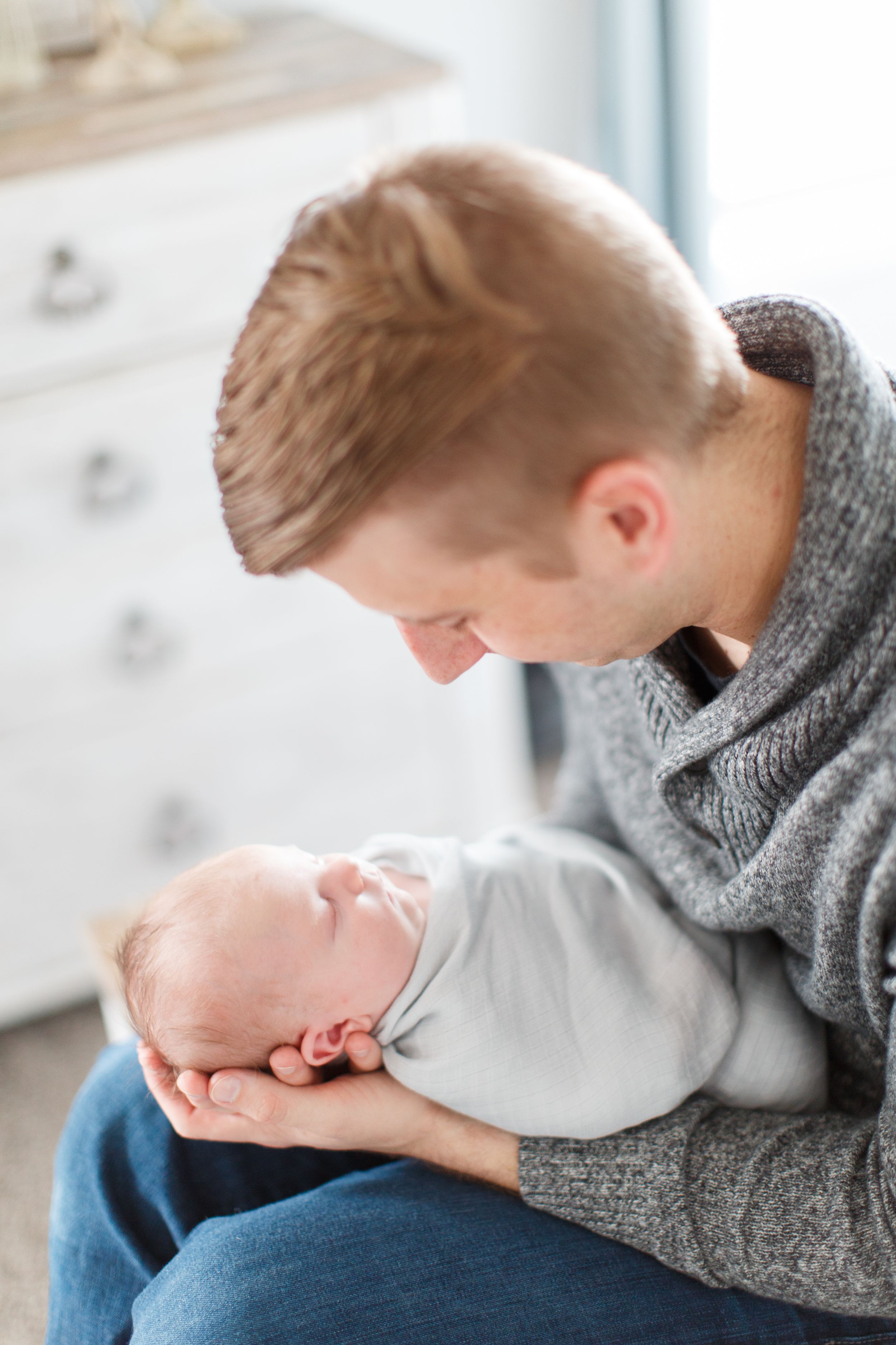 Gentle moment shared in bright nursery setting of father holding newborn during a lifestyle session in Springfield, Missouri.