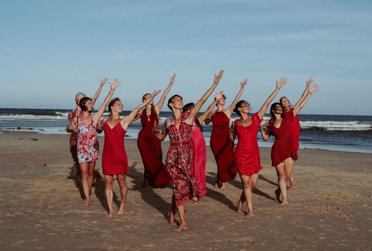 Group of people in red dresses celebrating on a beach with arms raised.