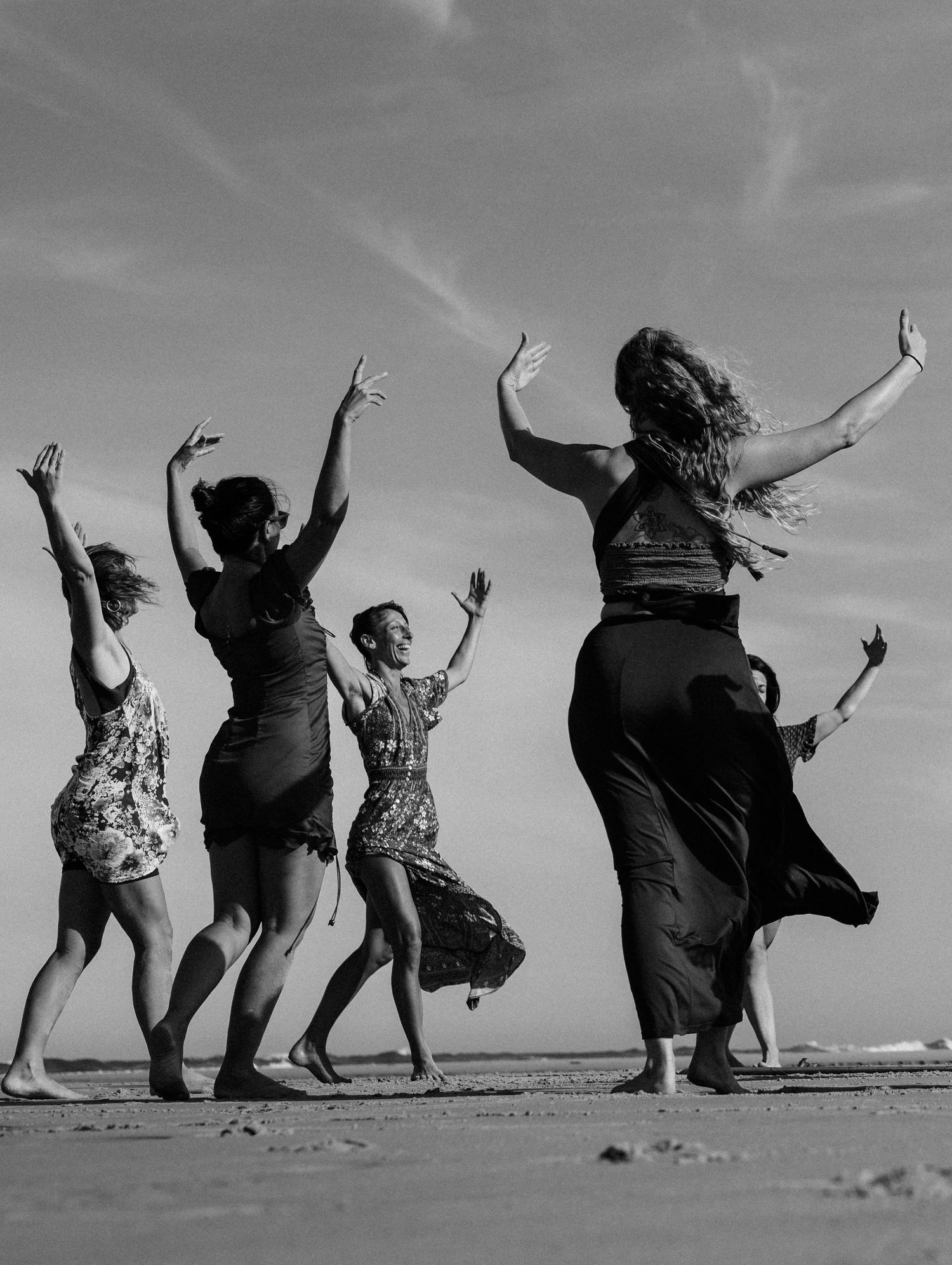 Silhouettes of people joyfully jumping on a beach against a dramatic sky.