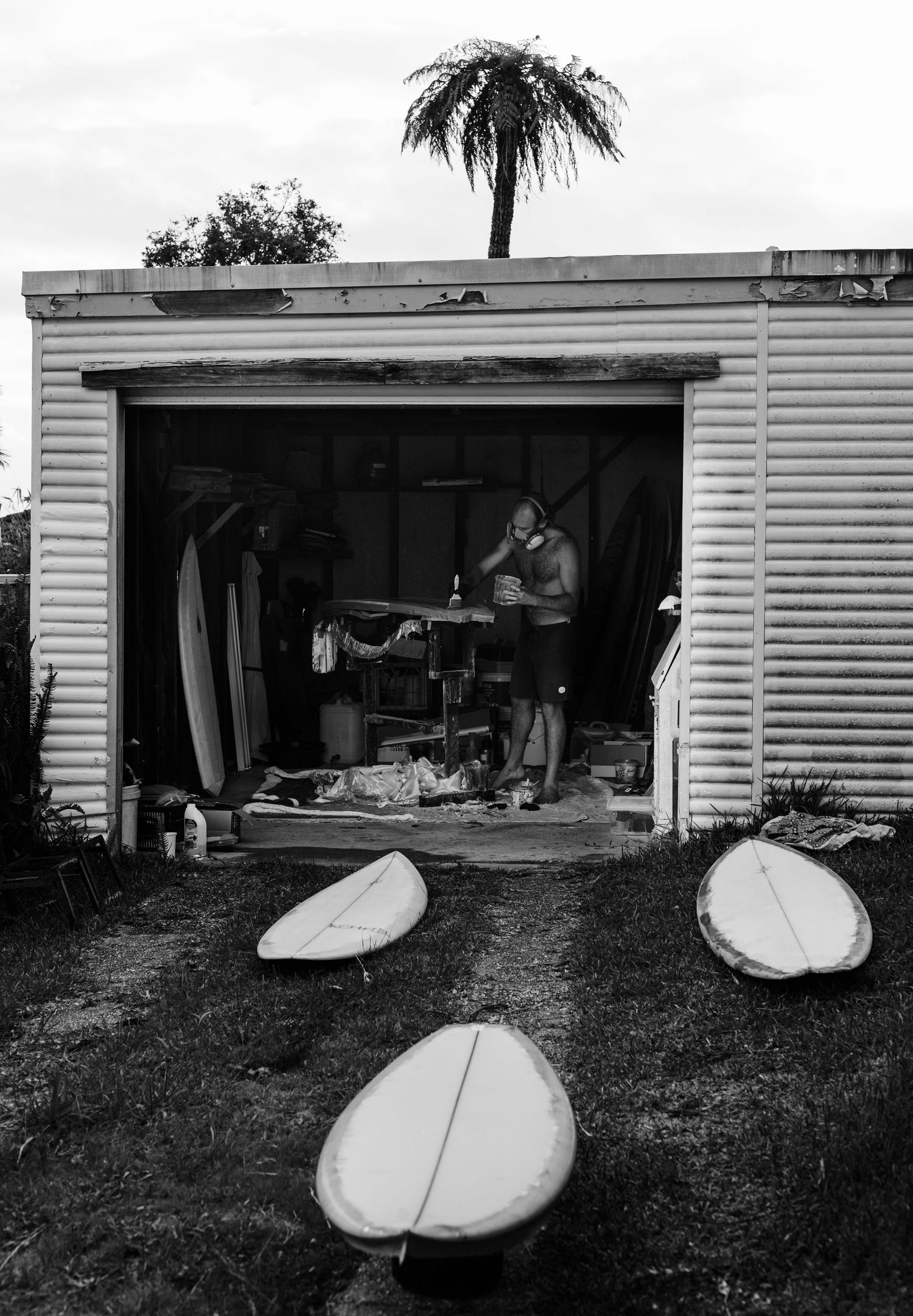 Multiple surfboards lined up outside a white garage or workshop building.