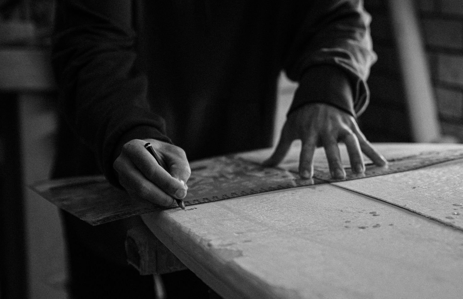 Close-up black and white shots of hands working on a wooden surface.