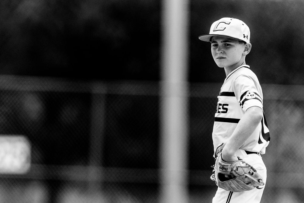 Black and white photo of a young boy in baseball uniform holding a glove during a little league game.