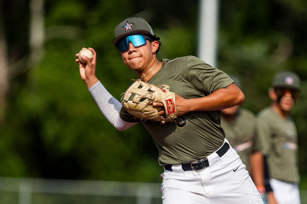 A baseball player in a gray uniform follows through on their swing during a game on a sunny day.
