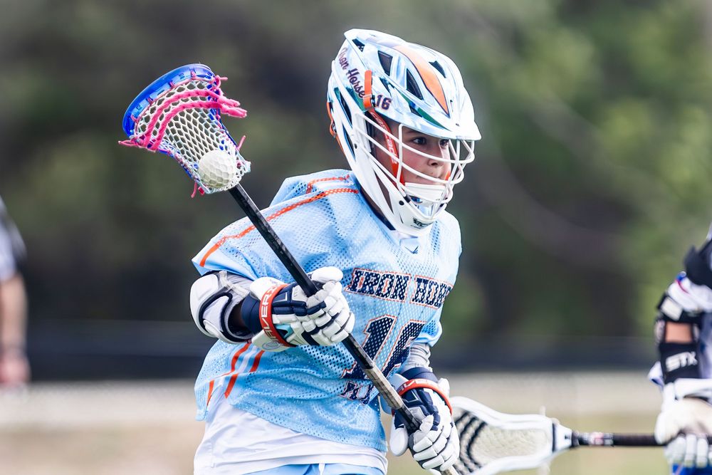 Lacrosse player in light blue uniform takes a shot during an intense game action moment.