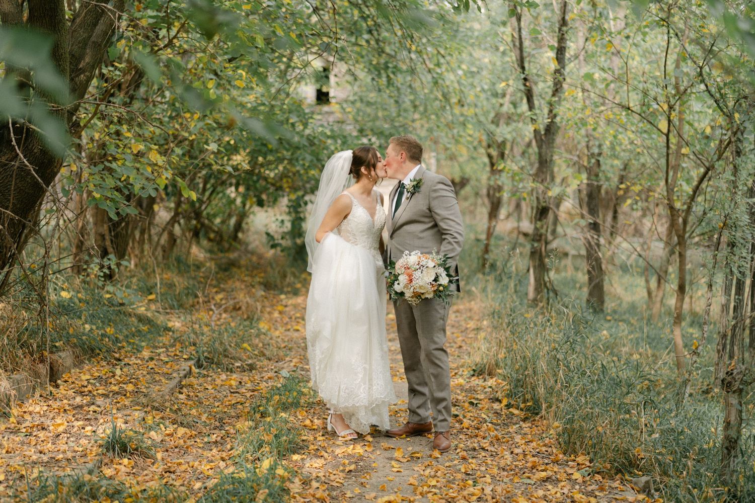 A bride and groom in Omaha, Nebraska share an intimate moment on a leaf-covered forest path during their autumn wedding.