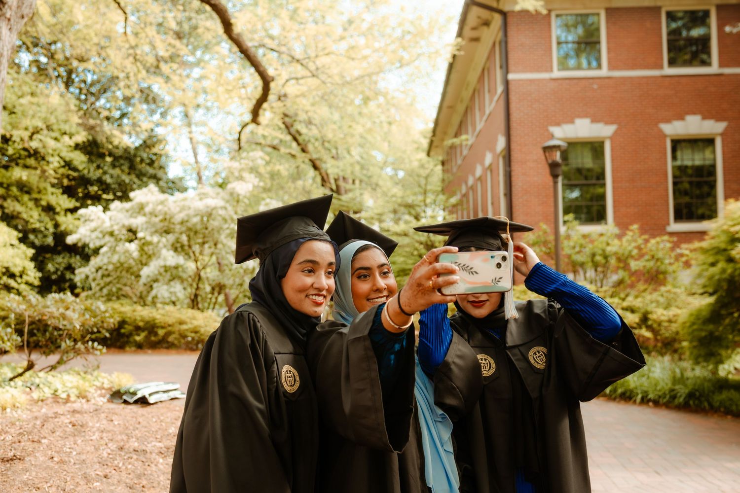 Graduates in academic regalia gather on steps of historic red brick building during commencement ceremony.