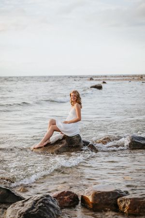 White dress flowing over coastal rocks as waves crash against the shore at sunset.