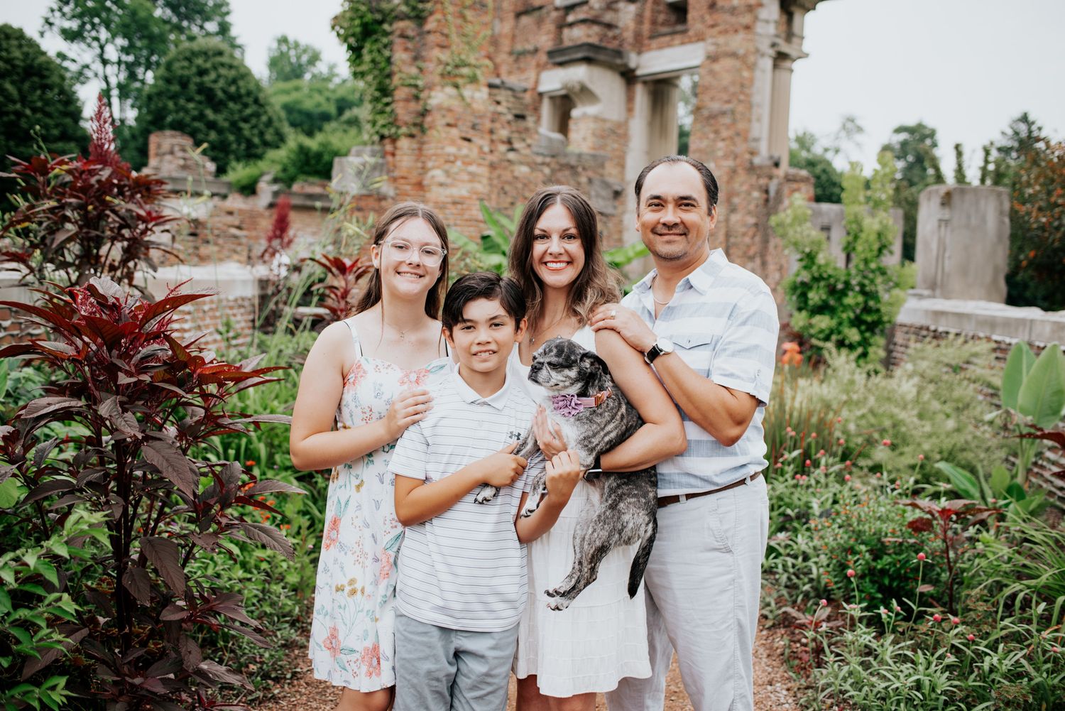 A family poses together in front of rustic stone ruins during a summer outdoor photo session.
