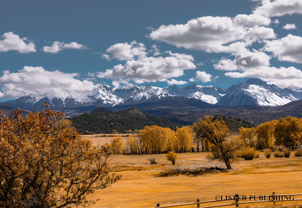 Scenic mountain landscape panorama with golden fields and snow-capped peaks.