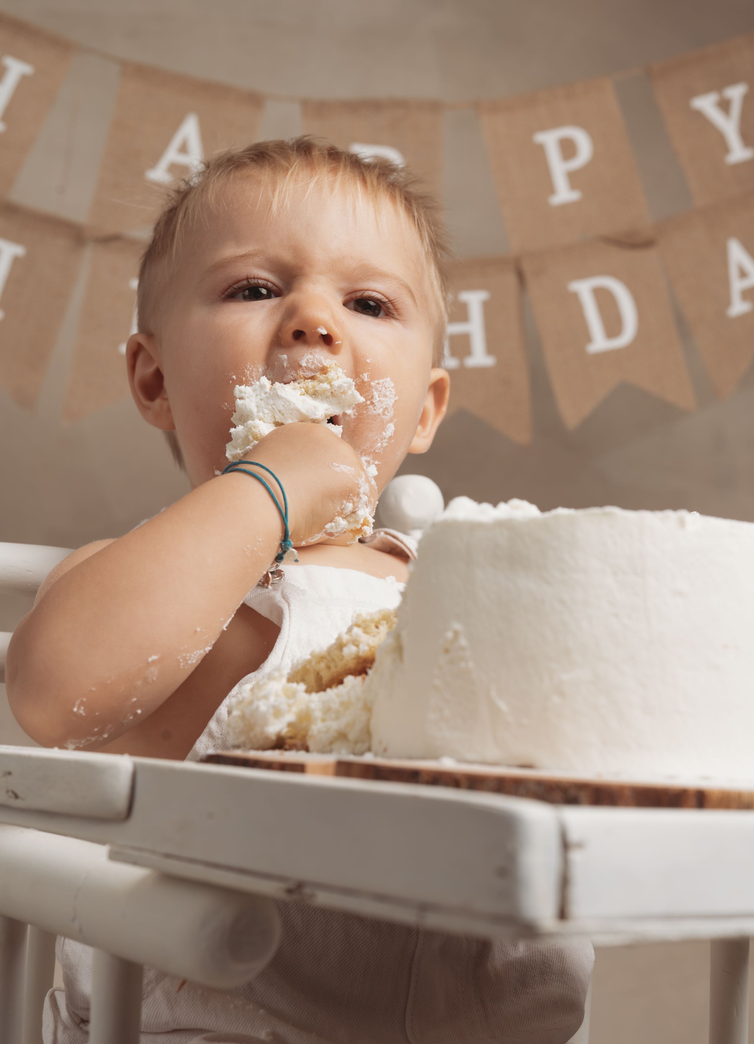 Baby smashing and eating birthday cake during first birthday cake smash photoshoot celebration.