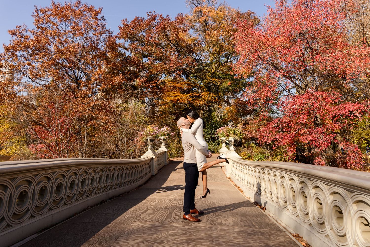 Couple sharing romantic moment on bridge with vibrant fall foliage in background.
