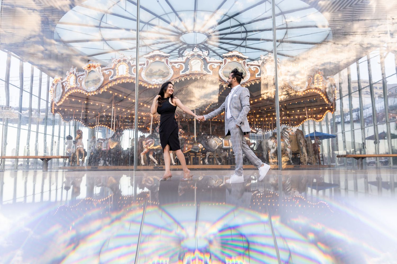 A couple dances playfully in front of an ornate vintage carousel in a dreamy indoor setting.