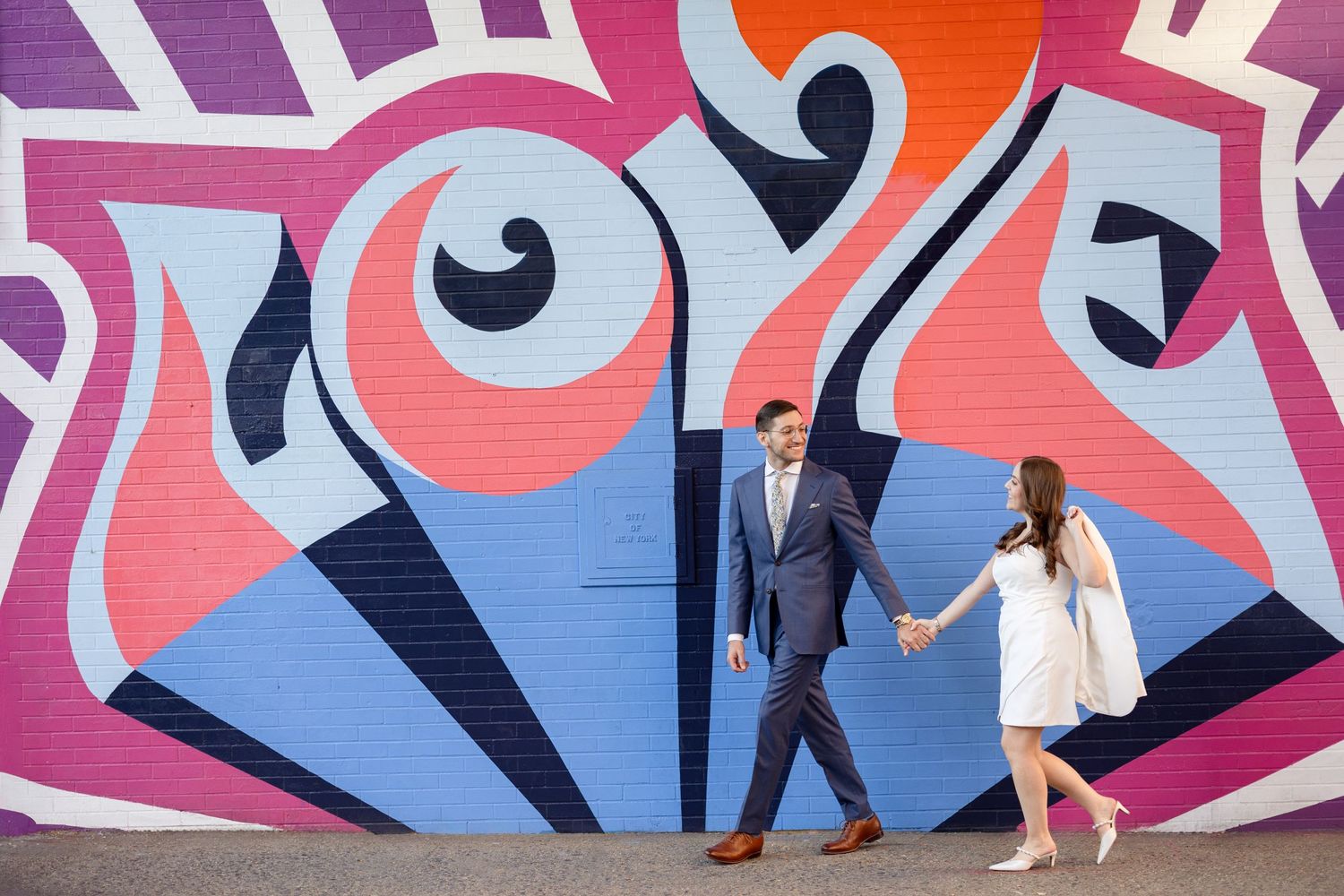 Stylish couple holding hands against colorful urban street art mural.