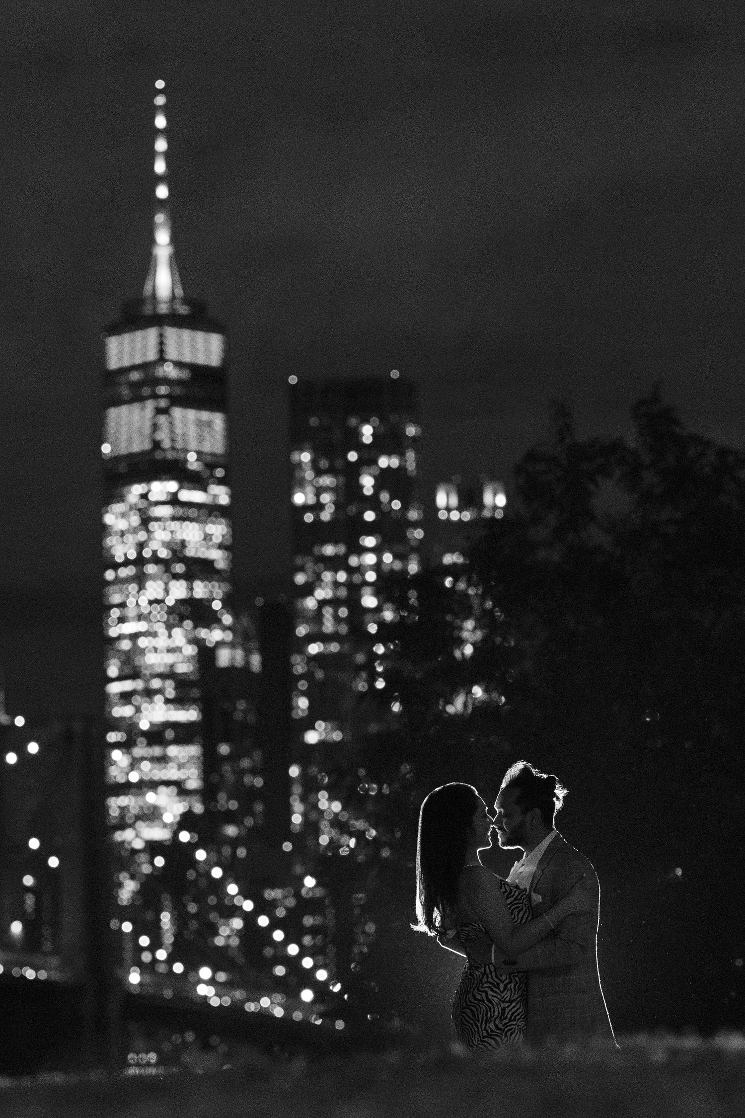 A romantic silhouette against the illuminated New York City skyline at night.