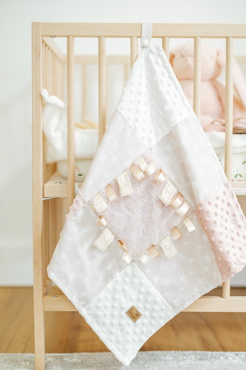 Delicate white minky blanket with decorative tags displayed on wooden crib.