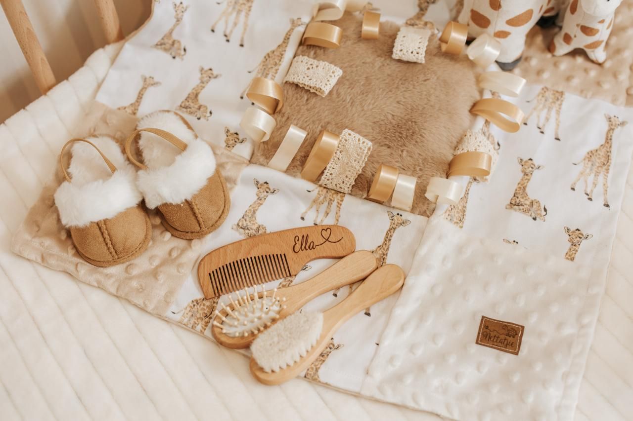 Tan baby shoes and giraffe patterned blanket arranged on white surface.