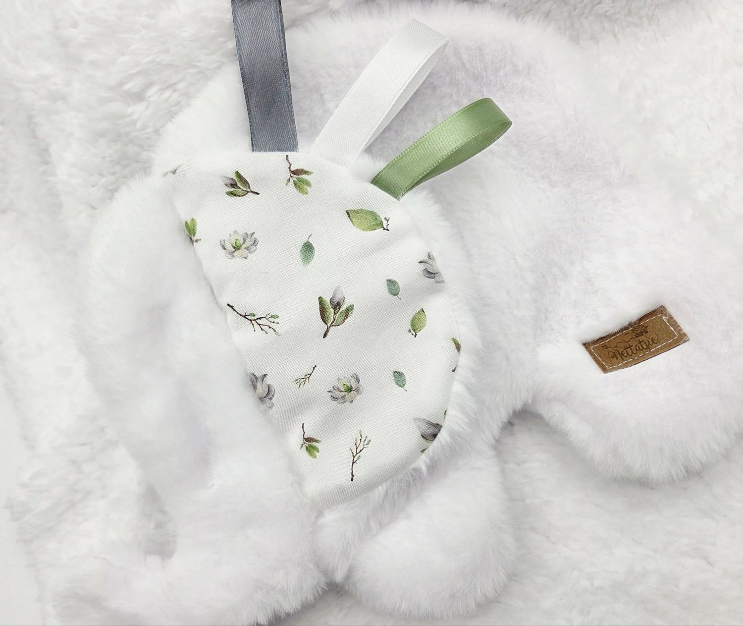 White and floral patterned baby accessories with green ribbon detail on soft background.
