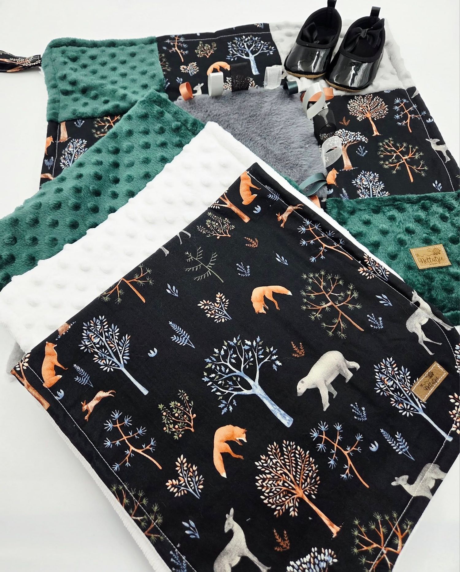 Baby blanket featuring woodland animals and trees pattern in black with green minky fabric backing.