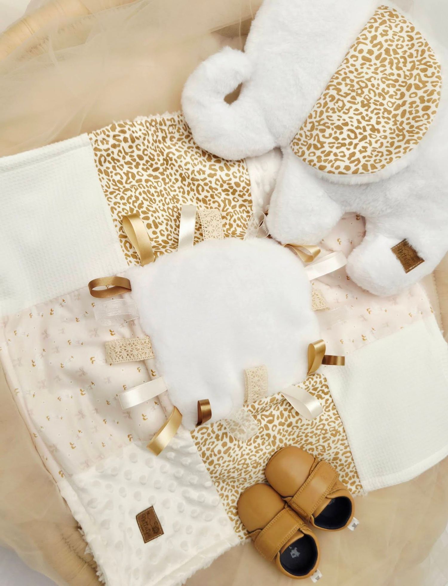 Gold leopard print baby gift set with plush elephant toy, taggie blanket, booties, and cream accessories.