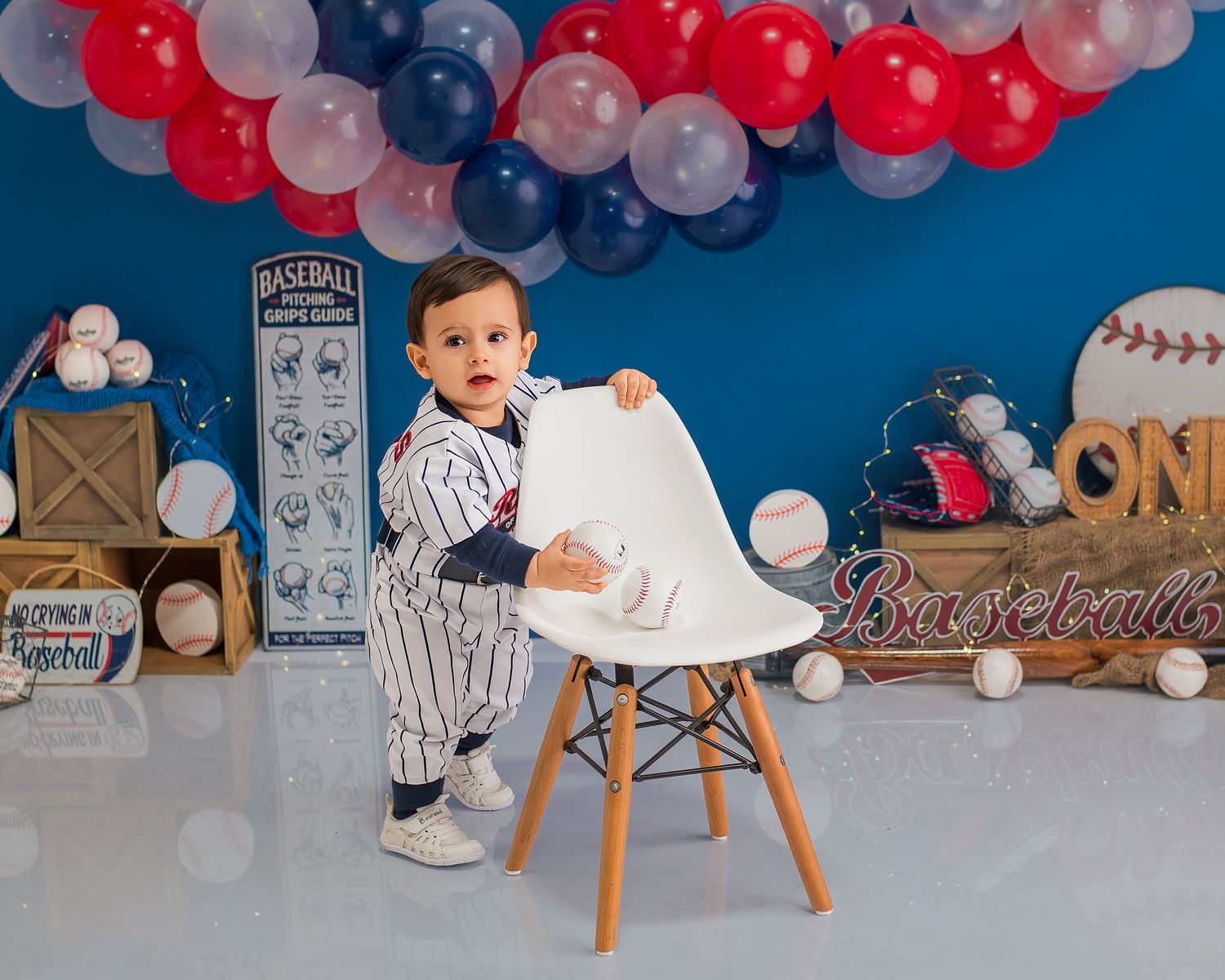 Red, white and blue balloon garland decorates a baby party setup against a navy blue backdrop.