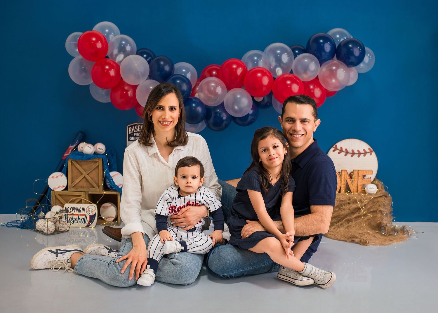 A series of photos showing a festive blue and red balloon display with people posing for first birthday portraits.