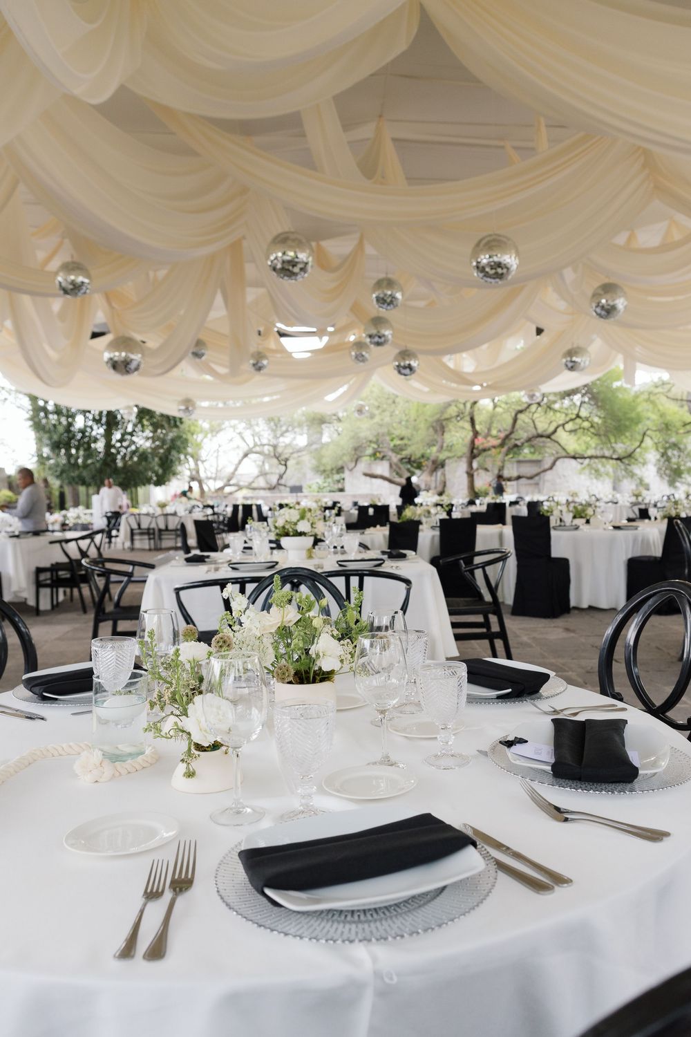 Elegant wedding reception tables with white linens, black accents, and draped ceiling decor.