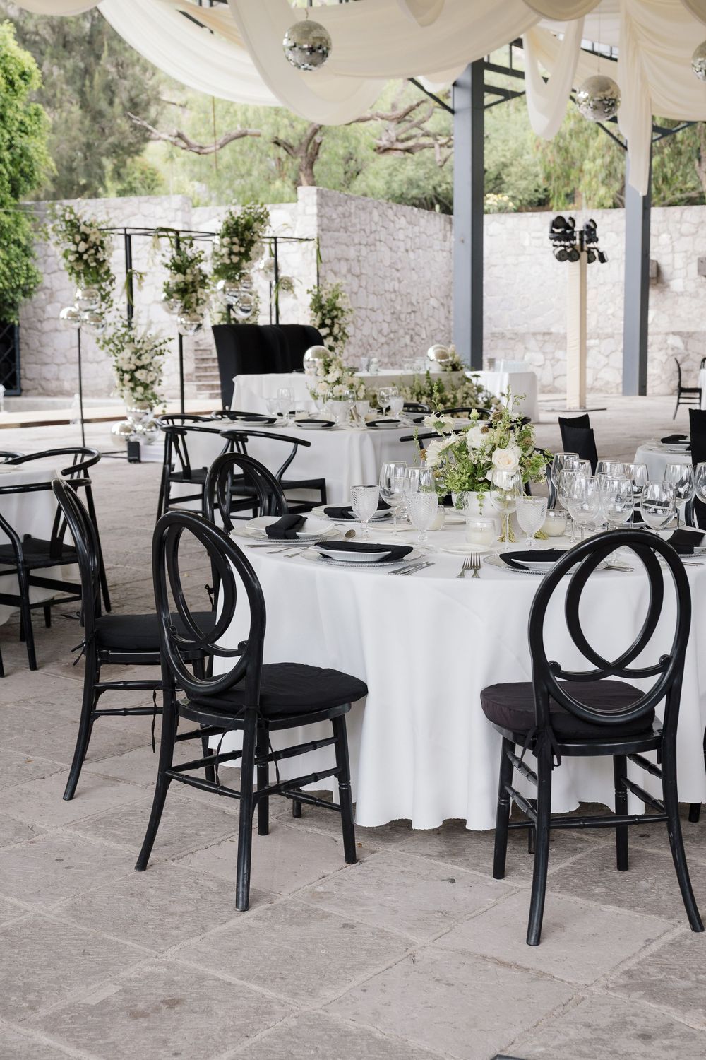 Black chairs and white tablecloths set up for outdoor wedding reception with stone walls.