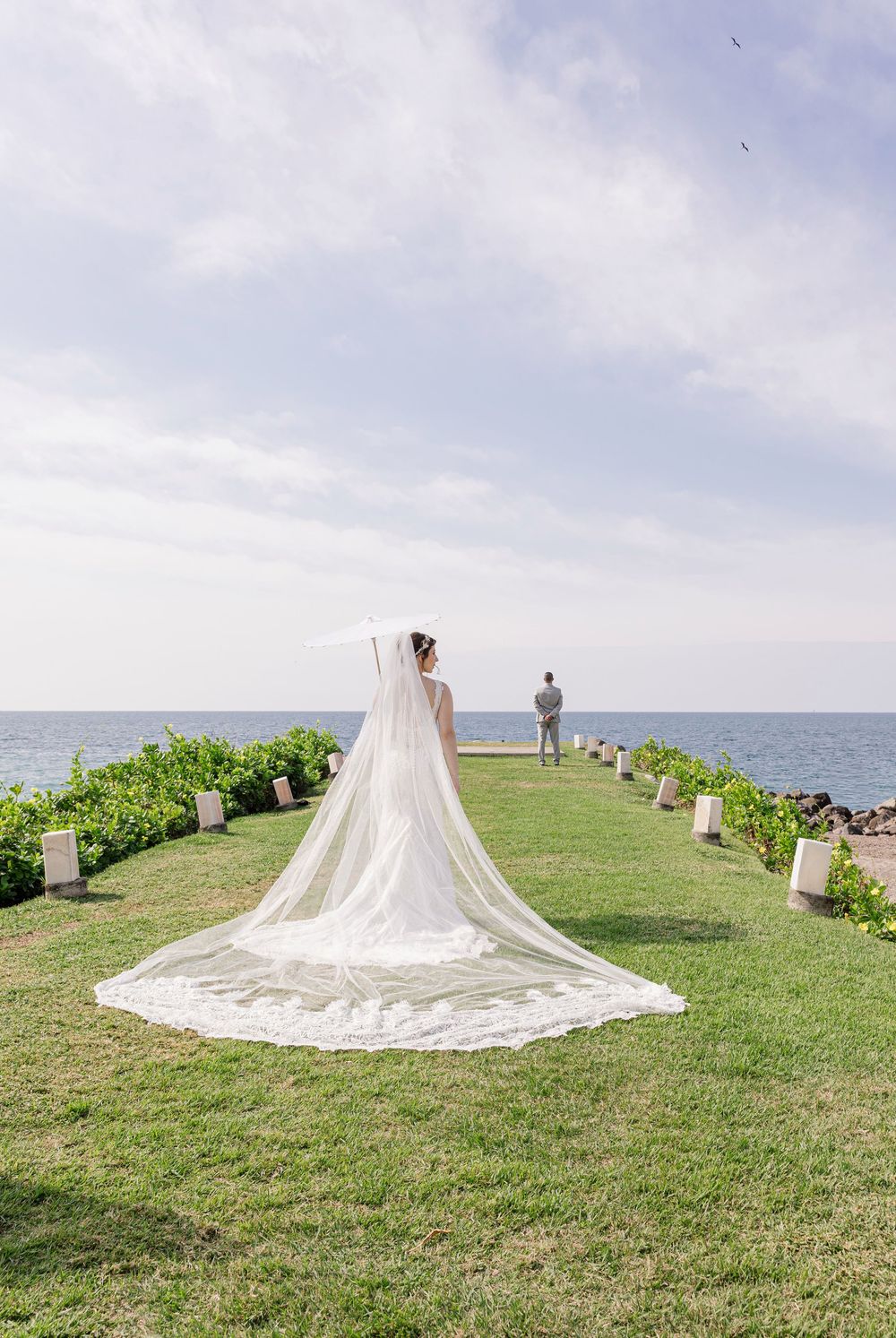 Un vestido de novia con un velo catedral fluido crea una silueta dramática contra el horizonte oceánico sobre un acantilado.