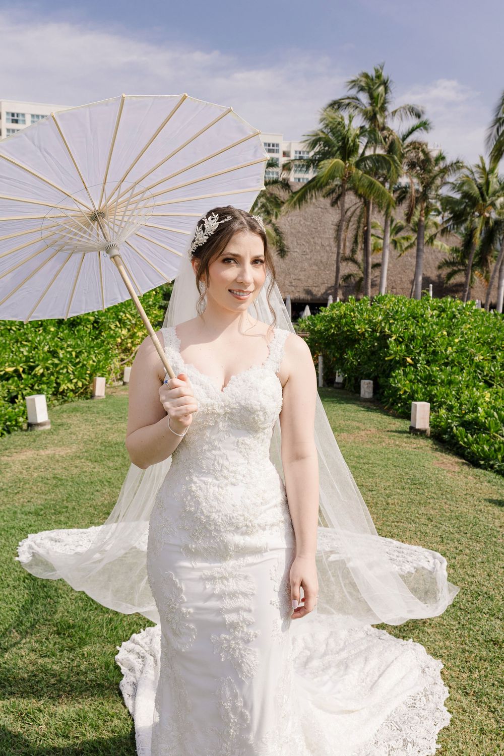 Un vestido de novia de encaje blanco con sombrilla en un jardín tropical crea una elegante escena nupcial.