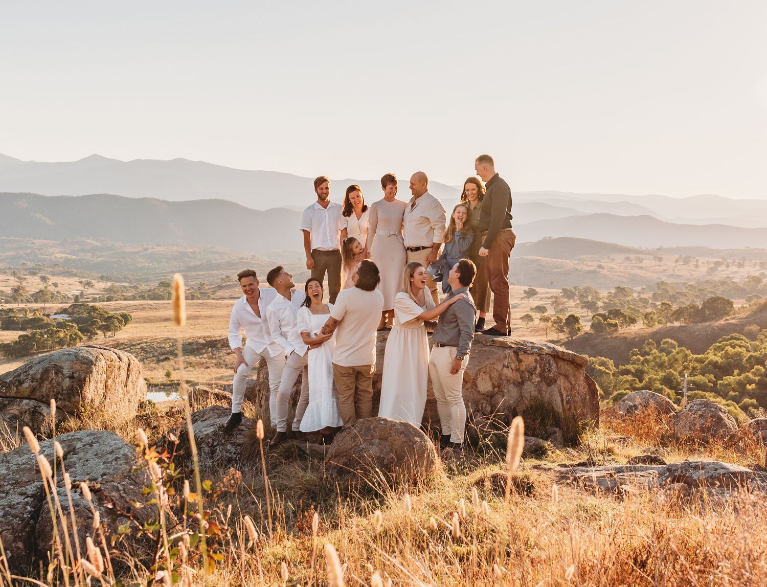 Group dressed in white gathered on rocky outcrop overlooking scenic mountain landscape at sunset.