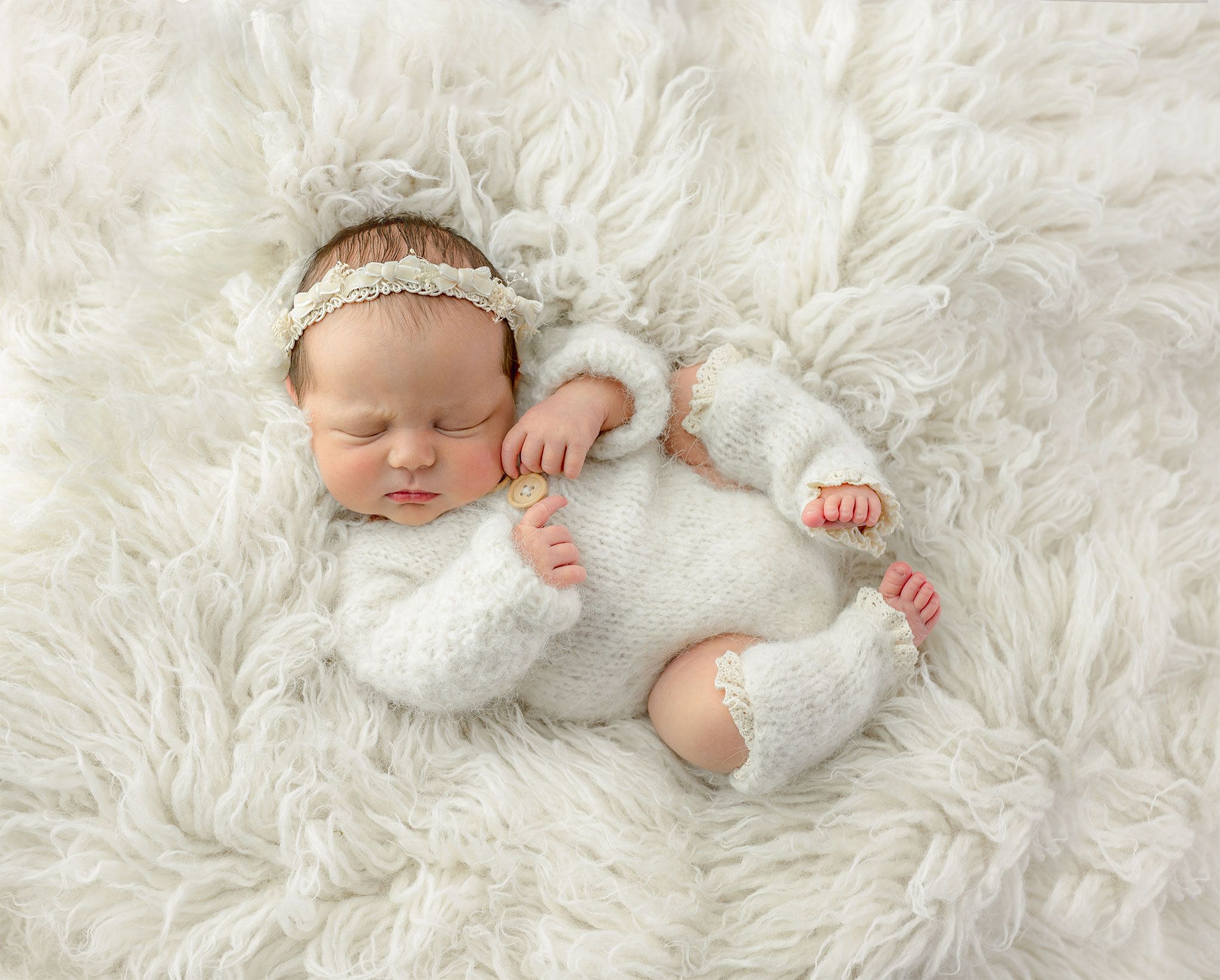 A sleeping newborn lies on soft white fur blanket in peaceful repose. Oban newborn photographer