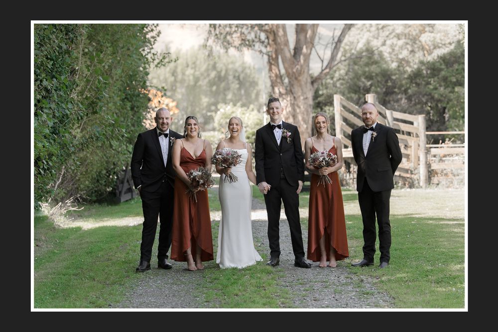 Wedding party poses together for formal portraits in an outdoor garden setting with lush greenery in the background.