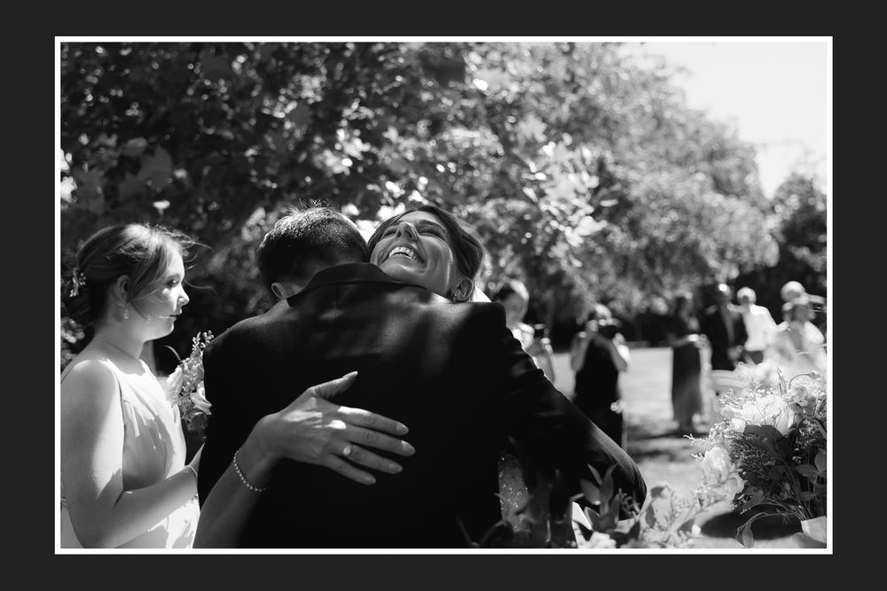 A black and white photograph captures an emotional embrace at what appears to be an outdoor gathering or event.