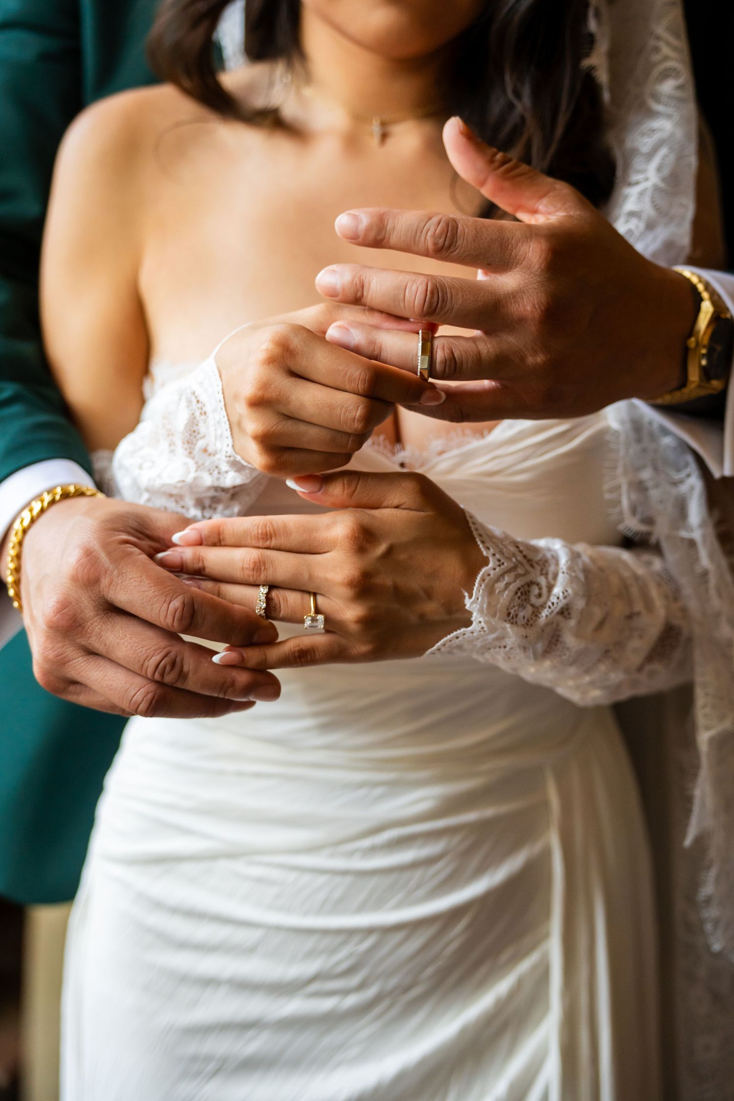 Close-up of newlyweds holding hands showing matching bracelets during wedding ceremony.