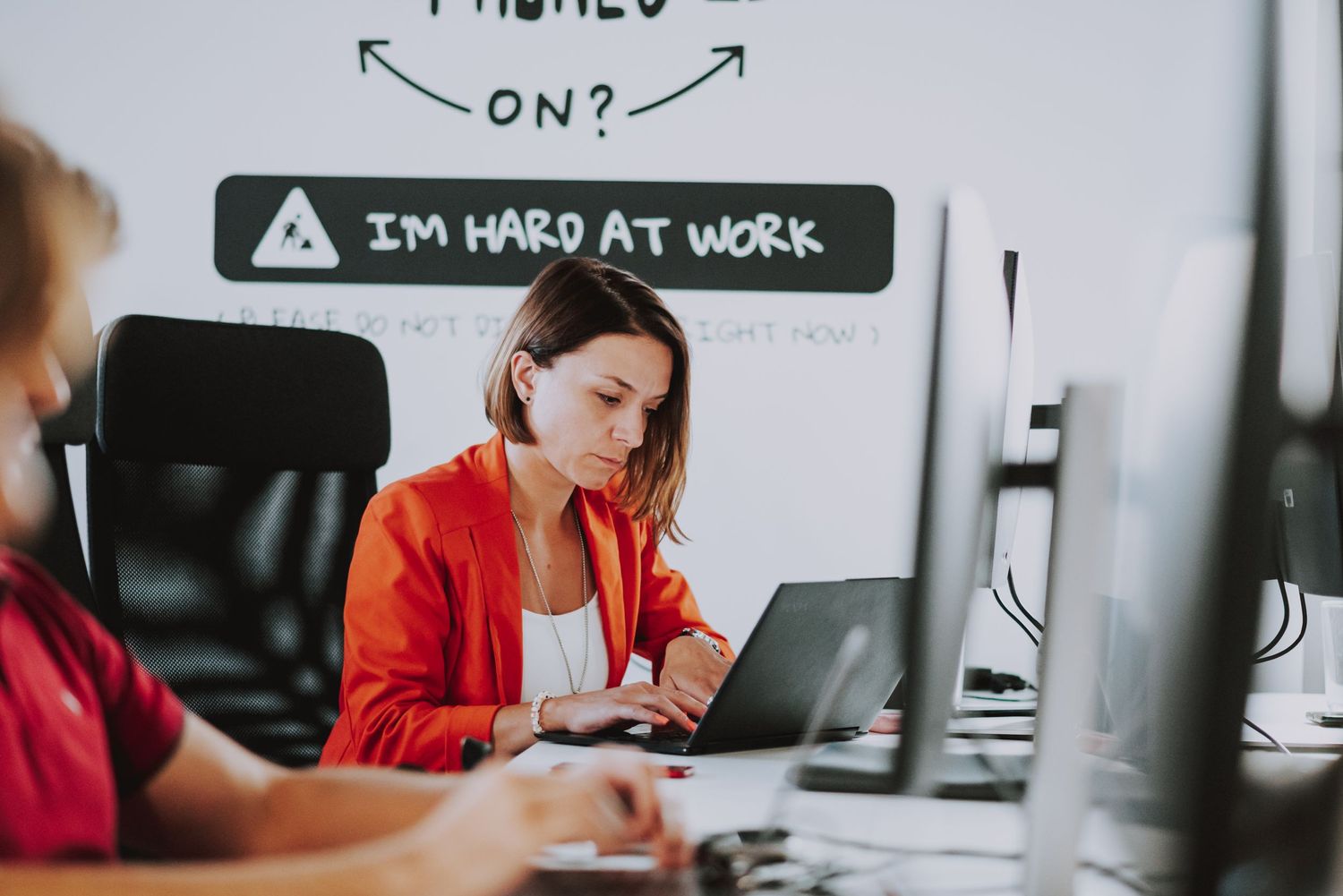 Office workers at desks with 'I'm hard at work' sign visible on wall.