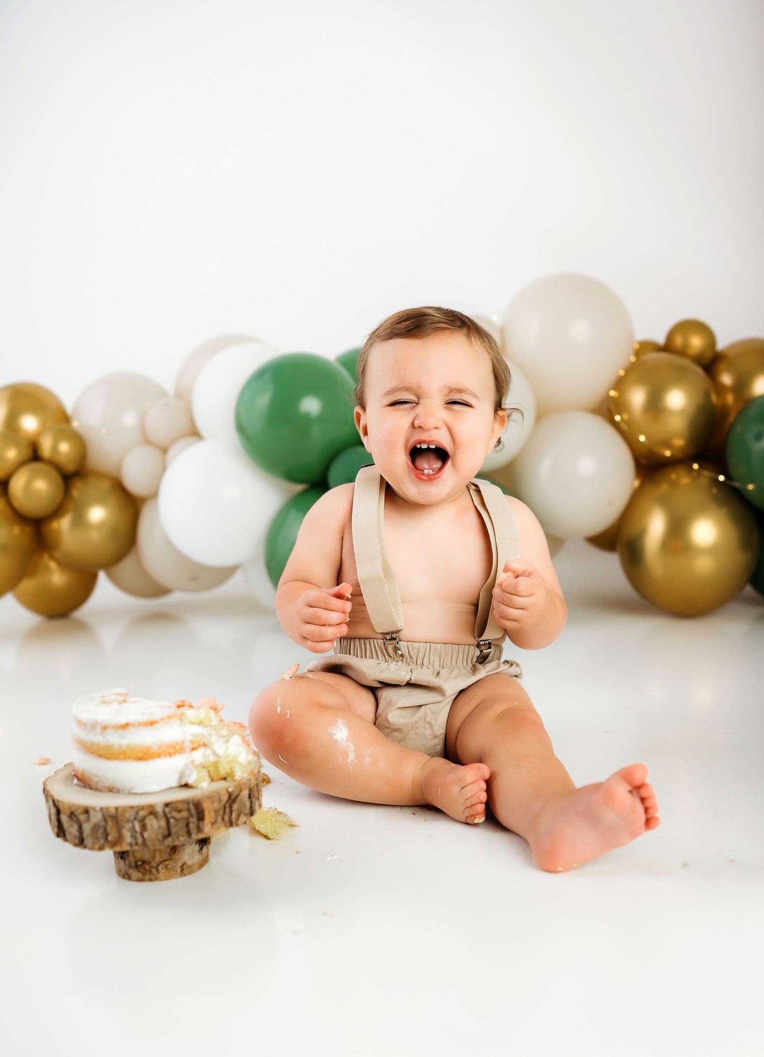 A baby wearing a dusty pink tulle dress sits in front of a neutral boho-styled backdrop with wooden decorative elements.