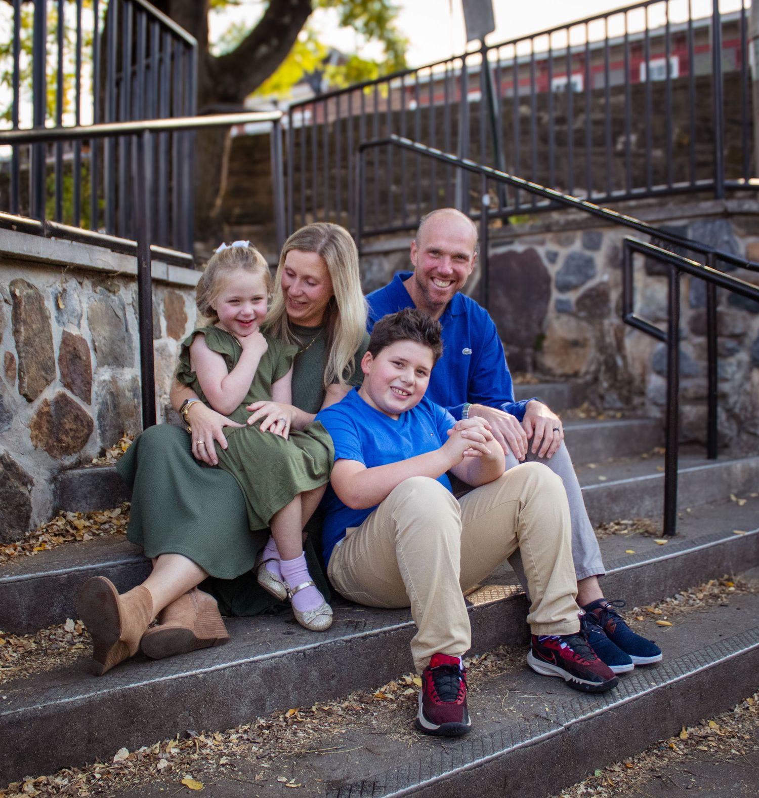 Family sitting together on stone steps outdoors during a fall photo session.