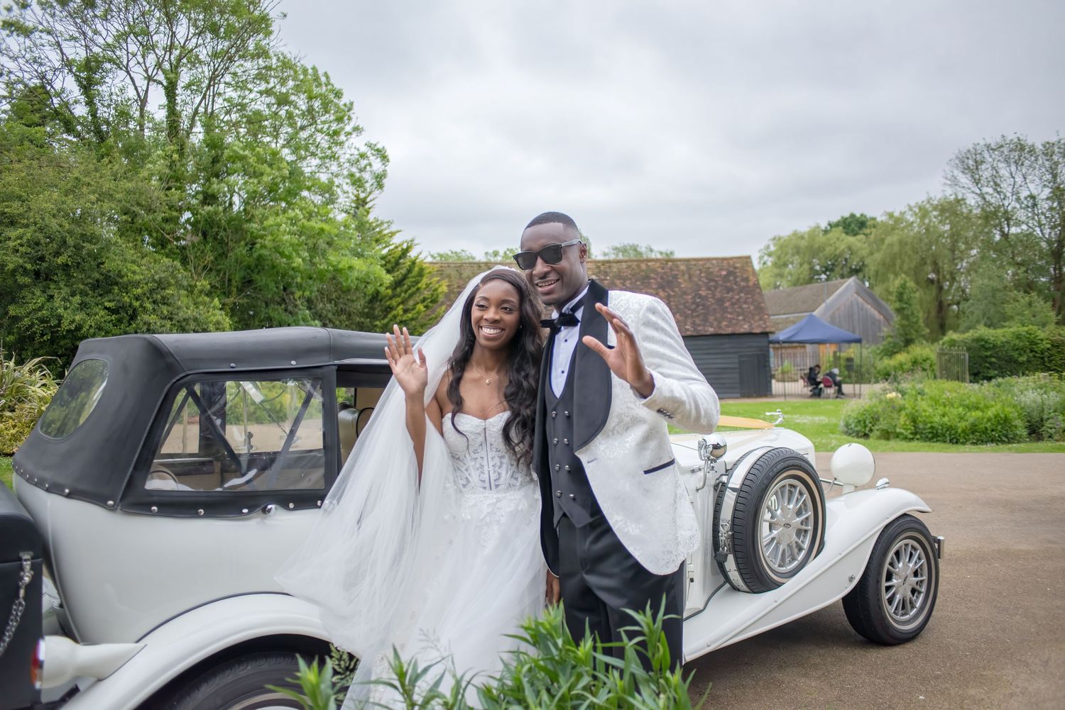 A classic vintage white wedding car parked on a driveway amid lush green gardens and trees.