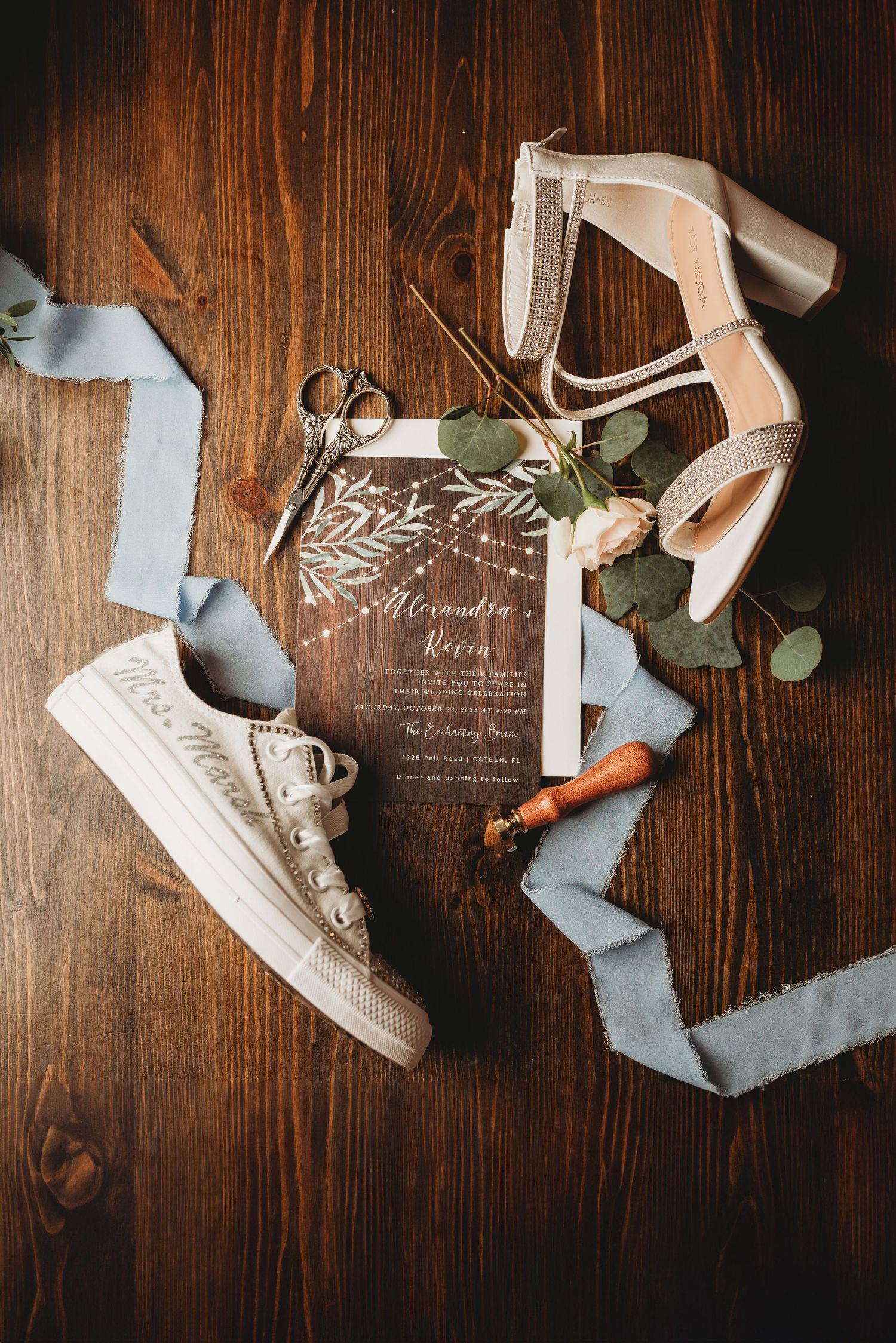 Wedding details flat lay with invitation, shoes, and blue ribbon on wooden background.