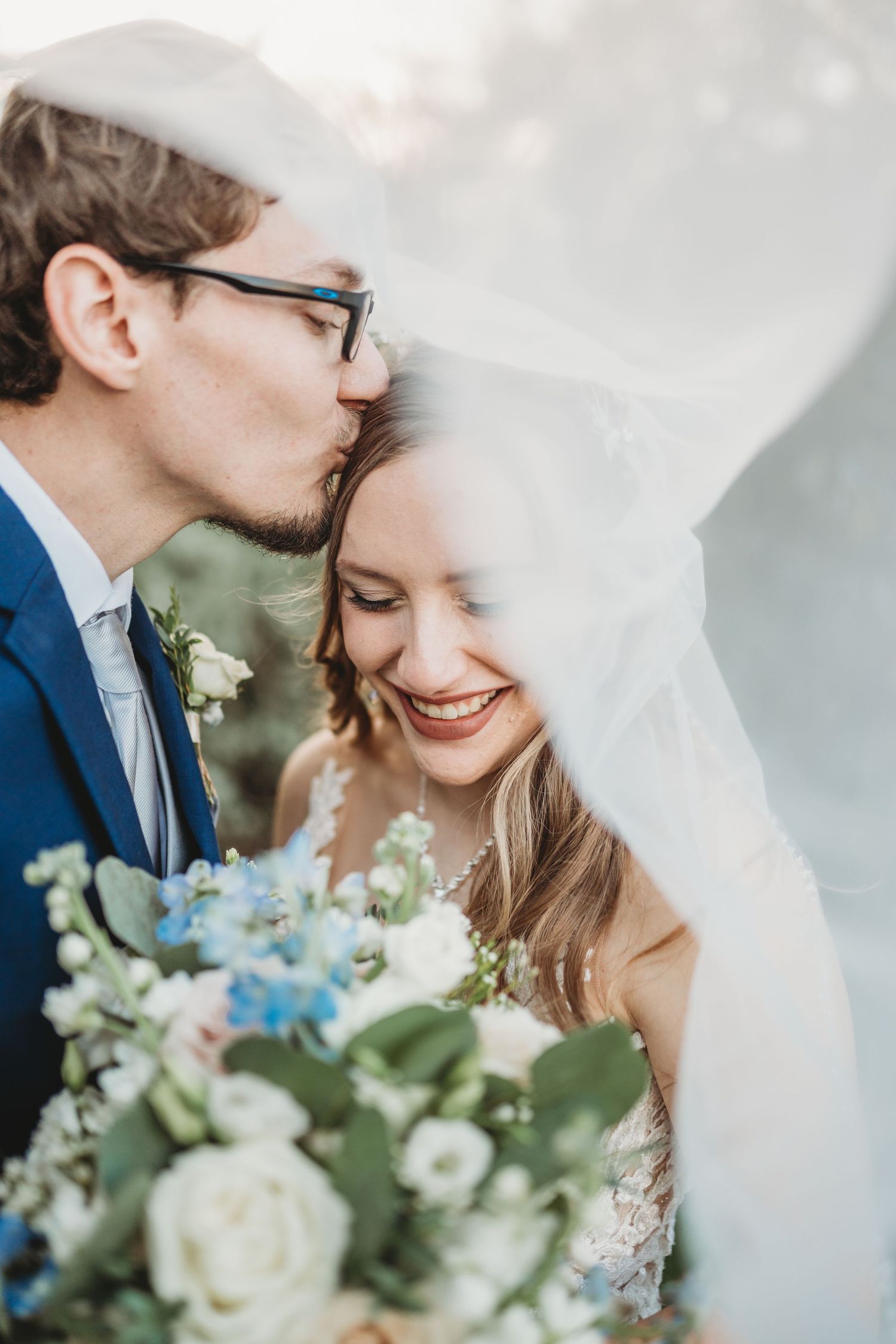 Intimate wedding portrait with blue and white bouquet under flowing veil.