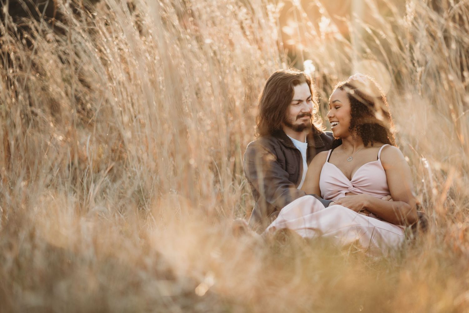A loving couple sharing an intimate moment while sitting together in a sunlit field of tall grass.