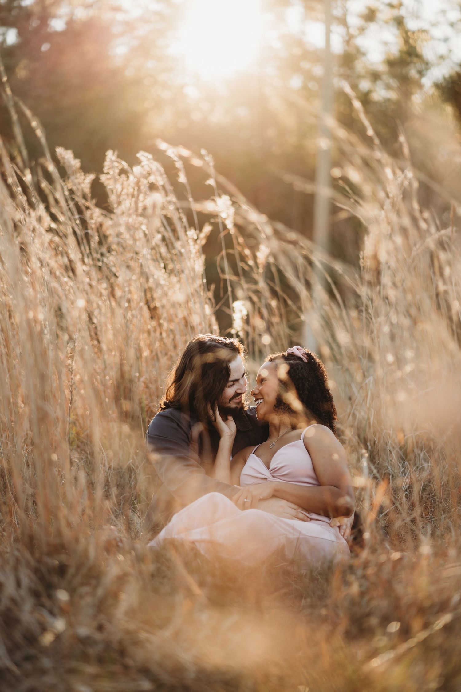 Maternity photo of couple sharing intimate moment in sunlit field of tall grass.