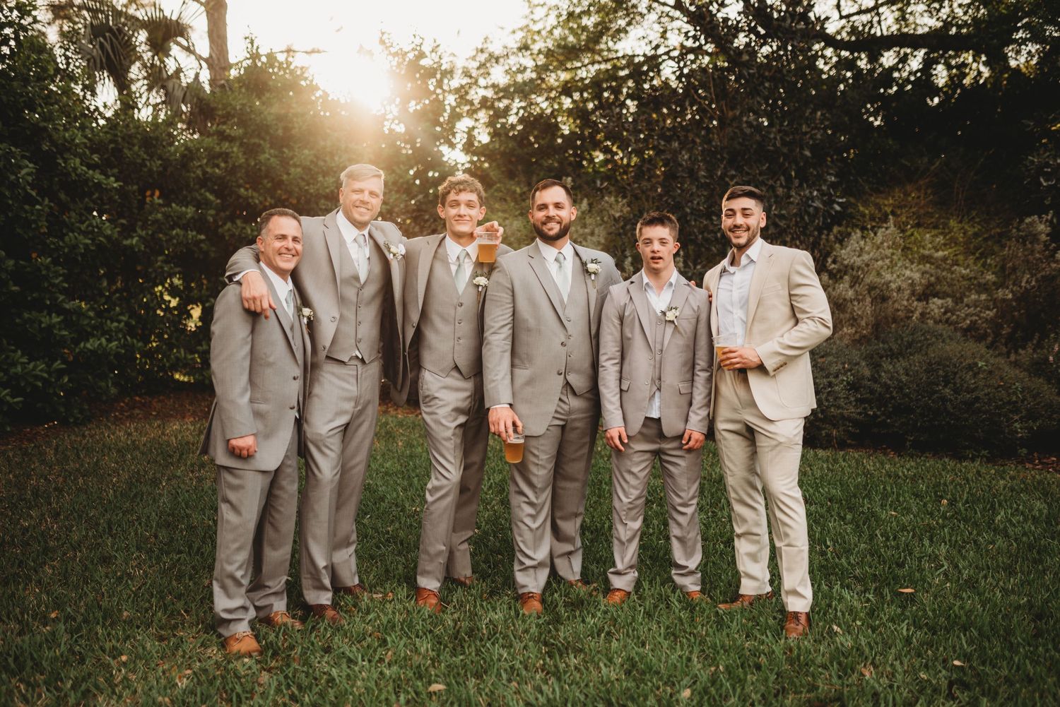 Groomsmen in light gray suits standing together outdoors against natural backdrop.