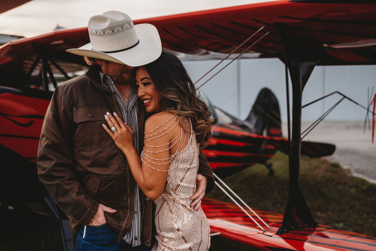 A couple shares an intimate moment next to a vintage red aircraft.