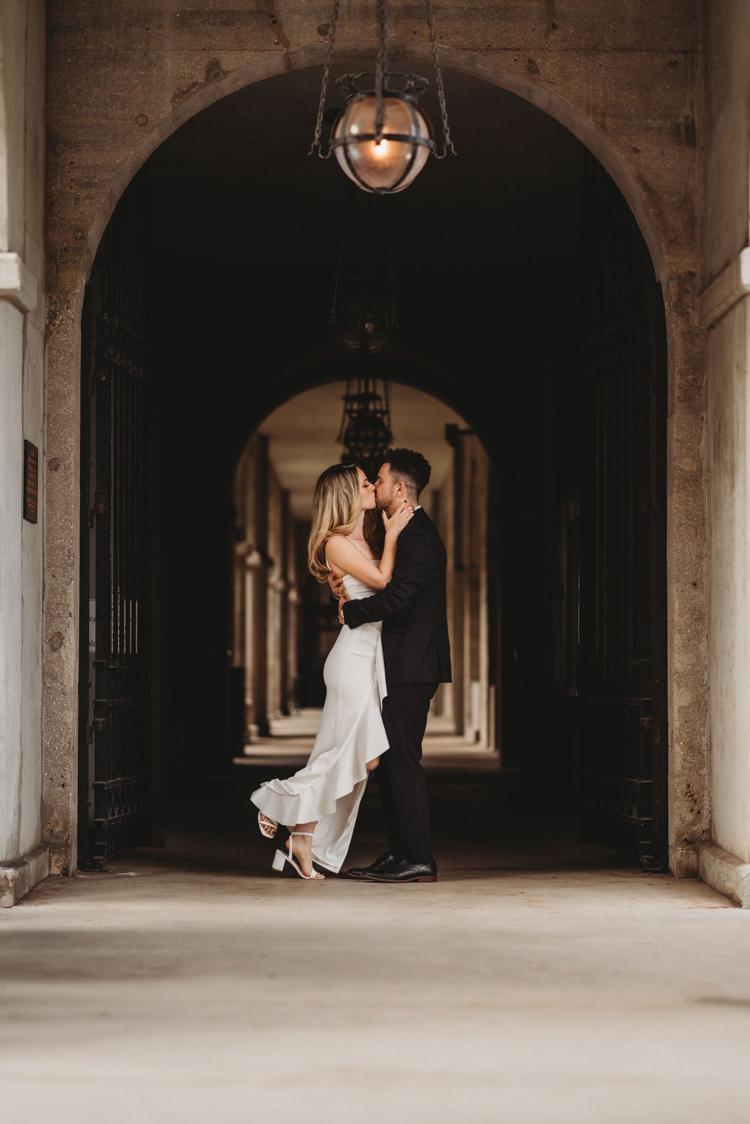 Romantic couple dancing under arched passageway with dramatic lighting.