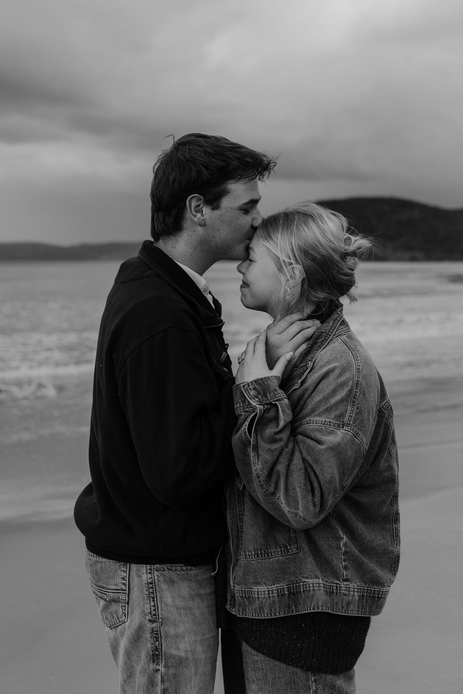 Black and white photo of a young couple smiling at each other in a grassy outdoor setting.