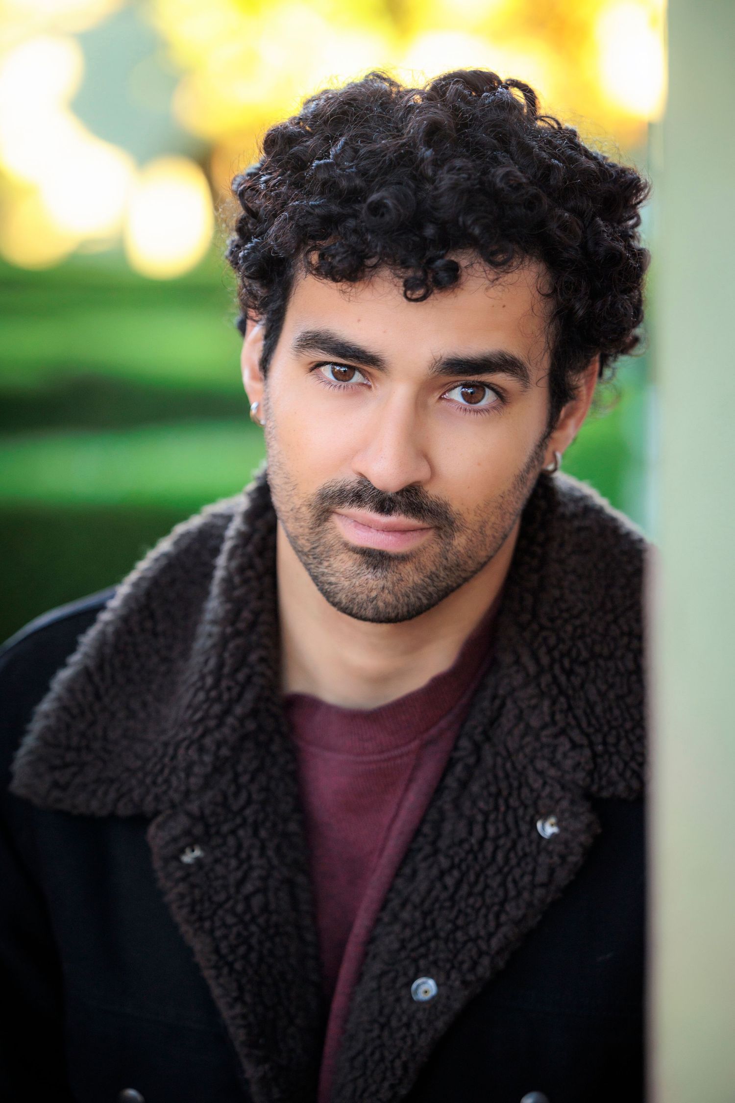 Handsome man with curly hair and beard wearing black shearling jacket outdoors in autumn.