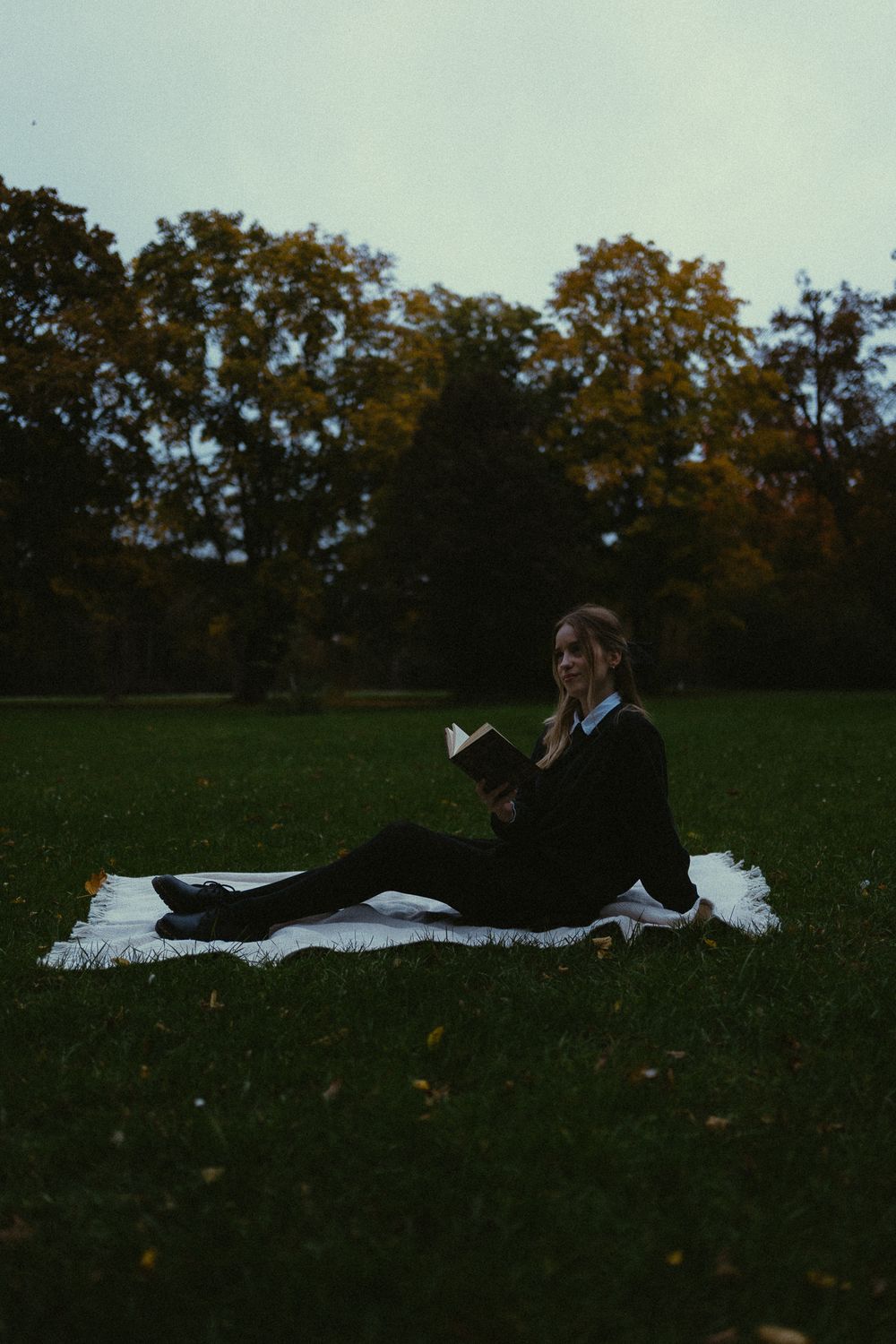 Junge Frau im Vintage Look liest ein Buch im Park im Grünen zur Blauen Stunde in Dresden