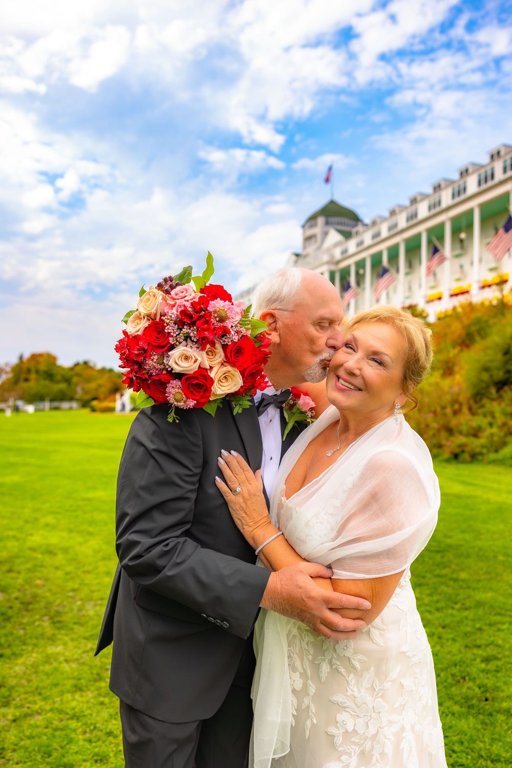 A joyful couple shares a romantic embrace on a grassy hill with a grand building in the background on their wedding day.