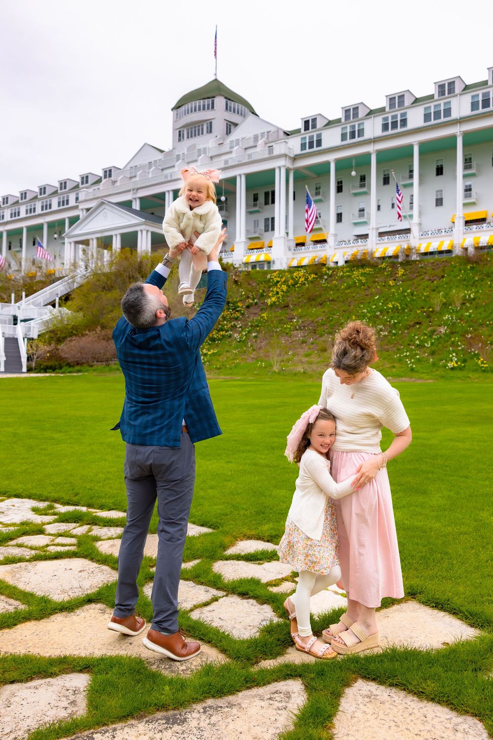 People pose playfully on stone steps leading up a grassy hill with a grand white hotel in the background.